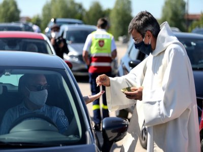 Un prêtre portant un masque de protection dépose une hostie dans la main d'un automobiliste garé sur un parking pour assister à une messe en plein air célébrée par Mgr François Touvet, l'évêque de Châlons-en-Champagne, le 17 mai 2020 - FRANCOIS NASCIMBENI [AFP]