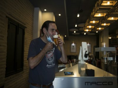 Le propriétaire du bar Gitana Loca, Alberto Martinez, boit une bière servie par un robot, le 17 mai 2020 à Séville, en Espagne - CRISTINA QUICLER [AFP]