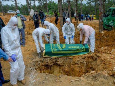 Des personnels funéraires en combinaison de protection enterrent une personne décédée du coronavirus en présence de la famille, le 21 mai 2020 à Istanbul, en Turquie - BULENT KILIC [AFP]