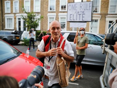 Dominic Cummings, le conseiller du Premier ministre Boris Johnson, à son arrivée chez lui à Londres, le 25 mai 2020, alors qu'une manifestante brandit une pancarte qui dit "Une règle à part pour les élites" - Tolga AKMEN [AFP]