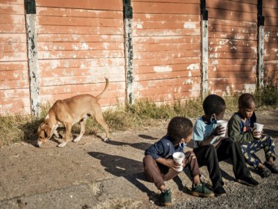 Des enfants assis par terre mangent du porridge distribué par une ONG, le 23 mai 2020 à Johannesburg, en Afrique du Sud - MARCO LONGARI [AFP/Archives]