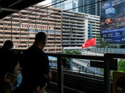 Des voyageurs sur le quai d'une station de métro à Hong Kong, avec le drapeau chinois en arrière-plan, le 29 mai 2020 - Anthony WALLACE [AFP]