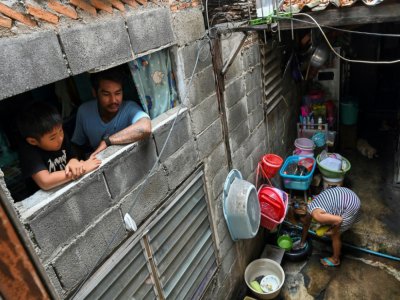 Thanapat Noidee et son fils à la fenêtre de la pièce qu'ils habitent dans un bidonville de Bangkok, le 30 mai 2020 en Thaïlande - Romeo GACAD [AFP]