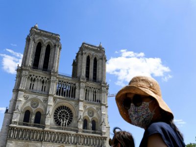 Une femme portant masque et chapeau se tient devant la cathédrale de Notre-Dame qui a rouvert au public, le 31 mai 2020 - ALAIN JOCARD [AFP]