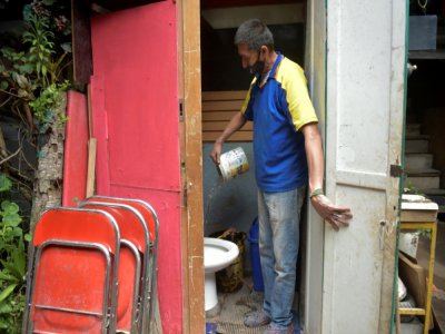 Jorge Ariza verse de l'eau dans la cuvette des toilettes de sa maison, construite de bric et de broc, le 26 mai 2020 à Bogota, en Colombie - Raul ARBOLEDA [AFP]