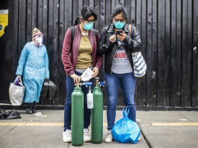 Deux femmes attendent une voiture pour aller remplir des bouteilles d'oxygène vides, le 3 juin 2020 à Lima, au Pérou - Ernesto Benavides [AFP]