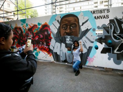Une femme, genou à terre et poing levé, devant une peinture murale représentant George Floyd, le 11 juin 2020 à Graffiti Alley, à Toronto - Cole BURSTON [AFP]