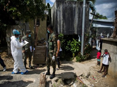 Un soldat monte la garde pendant qu'un employé du ministère de la Santé effectue des tests du coronavirus à San Cristobal, en République dominicaine, le 13 juin 2020 - Erika SANTELICES [AFP]
