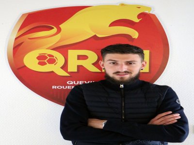 Robin Taillant pose devant le logo de son nouveau club, le Quevilly Rouen Métropole. - QRM