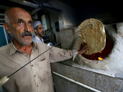 Le boulanger iranien Amir Jafari, 58 ans, sort un pain taftoun du four de sa boulangerie, à Téhéran, le 13 juin 2020 - ATTA KENARE [AFP]