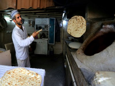 Mohammad Mirzakhani, un boulanger iranien, sort du four de sa boulangerie un pain taftoun, à Téhéran, le 13 juin 2020 - ATTA KENARE [AFP]