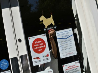 Une employée de la Croix-Rouge britannique place le panneau "ouvert" sur la vitrine d'un magasin, le 25 juin 2020 à Londres - JUSTIN TALLIS [AFP]