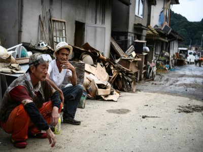 Des hommes sont assis dans une rue bordée d'objets détruits par les pluies et les inondations, entassés dans l'attente des éboueurs, à Hitoyoshi au Japon le 8 juillet 2020 - CHARLY TRIBALLEAU [AFP]
