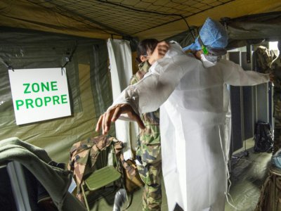Une militaire aide un collègue à enfiler une blouse de protection sans la contaminer, le 24 mars 2020 à l'hôpital de campagne destiné à accueillir les malades du Covid-19, à Mulhouse - SEBASTIEN BOZON [POOL/AFP/Archives]