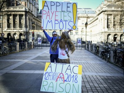 L'activiste français Jean-Baptiste Redde, brandit une pancarte sur laquelle on peut lire "Apple, paie tes impôts", le 12 février 2018 à Paris - STEPHANE DE SAKUTIN [AFP]