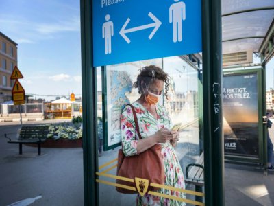 Une passante à Stockholm, le 26 juin 2020 devant une affiche recommandant la distanciation sociale - Stina STJERNKVIST [TT NEWS AGENCY/AFP]