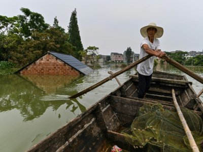 Un pêcheur passe en barque près d'une habitation dont n'émerge que le toit, dans le village de Longkou, dans la région de Poyang qui a subi des pluies violentes, dans la province du Jiangxi, au centre de la Chine, le 16 juillet 2020 - Hector RETAMAL [AFP]