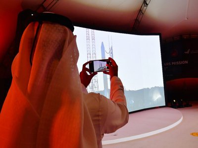 Un homme prend une photo de l'écran montrant le lancement de la sonde émiratie Al-Amal en route pour Mars depuis le Japon, le 19 juillet 2020 au Centre spatial Mohammed bin Rashid (MBRSC) de Dubaï - Giuseppe CACACE [AFP]