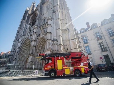 Un policier se promène devant un véhicule des pompiers stationné devant la façade partiellement brûlée de la cathédrale Saint-Pierre-et-Saint-Paul de Nantes, dans l'ouest de la France, le 20 juillet 2020 - Loic VENANCE [AFP]