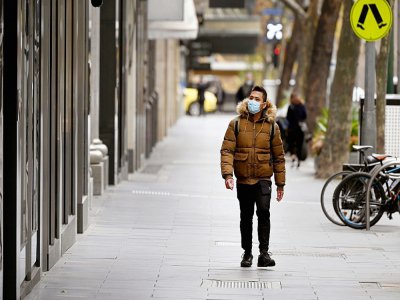 Un homme portant un masque descend Collins Street, dans un quartier commercial normalement bondé de Melbourne, dans l'Etat de Victoria, où ont été recensés la plupart des  502 nouveaux cas de coronavirus annoncés mercredi par l'Australie - William WEST [AFP]