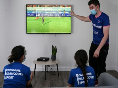 Un animateur donne des instructions à deux filles jouant au jeu vidéo Fifa lors d'un stage gratuit, le 22 juillet 2020 à Boulogne-Billancourt - BERTRAND GUAY [AFP]