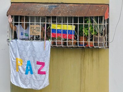 Une femme salue depuis sa fenètre à l'écoute de l'émission de Ruben Pena, qui diffuse depuis le toit de son immeuble des chansons pour égayer la vie des habitants, à Caracas, le 18 juillet 2020 - Federico PARRA [AFP]
