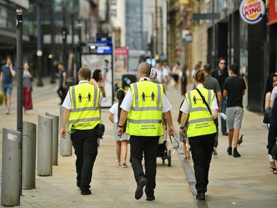 Des agents du réseau de transports en commun de Manchester au nord-ouest de l'Angleterre portent des gilets fluorescents invitant les usagers à respecter les distances physiques lors de l'épidémie de Covid-19 le 31 juillet 2020 - Oli SCARFF [AFP]
