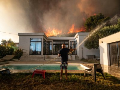 Un homme tente de maitriser le feu avant d'être évacué de sa maison à La Couronne, près de Marseille le 4 août 2020 où un violent incendie ravage l'ouest de la ville - Xavier LEOTY [AFP]