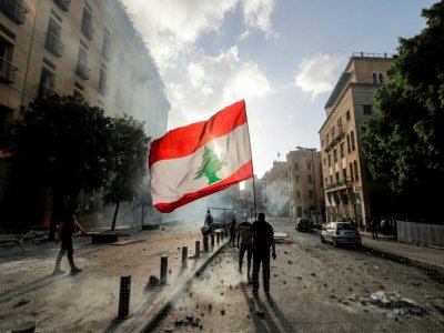 Un protestataire à Beyrouth brandit le drapeau national libanais devant les forces de sécurité pendant une manifestation le 8 août après l'explosion dévastatrice du 5 août - JOSEPH EID [AFP]