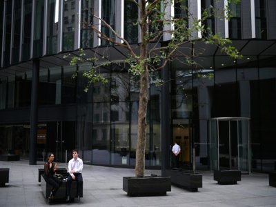 De rares employés de bureaux sont assis à l'extérieur d'un immeuble dans les rues désertées de la City à Londres, pendant l'épidémie de coronavirus le 6 août 2020 - DANIEL LEAL-OLIVAS [AFP]