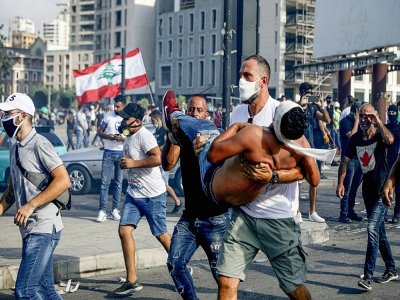 La star du basketball au Liban Fadi al-Khatib transporte en courtant un manifestant blessé lors des manifestations à Beyrouth contre le pouvoir, le 8 août 2020 - PATRICK BAZ [AFP]