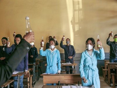 Des étudiants brandissent des bouteilles de Covid Organics, une tisane à base de plantes présentée comme un remède au coronavirus par le président malgache Andry Rajoelina, à Antananarivo loe 23 avril 2020 - RIJASOLO [AFP]