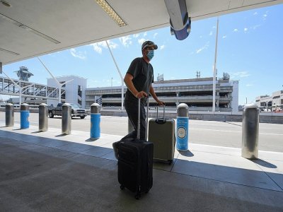 Un homme portant un masque pousse ses bagages à l'aéroport international de Los Angeles le 12 août 2020 pendant l'épidémie de coronavirus - Robyn Beck [AFP]