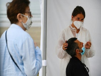 Une infirmière fait un prélèvement sur un patient dans un centre mobile de dépistage du coronavirus, sur la plage de Pentrez à Saint-Nic, dans l'ouest de la France le 12 août 2020 - Fred TANNEAU [AFP]