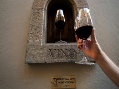 Une personne tient un verre de vin à côté d'une "fênêtre à vin" dans une rue de Florence, le 12 août 2020 en Italie - Tiziana FABI [AFP]