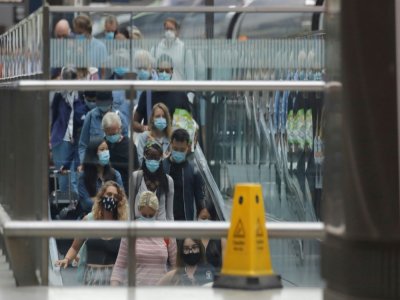 Des voyageurs, portant des masques de protection, prennent un escalator à leur descente de l'Eurostar en provenance de Paris, le 14 août 2020 à la gare St Pancras de Londres - Tolga AKMEN [AFP]
