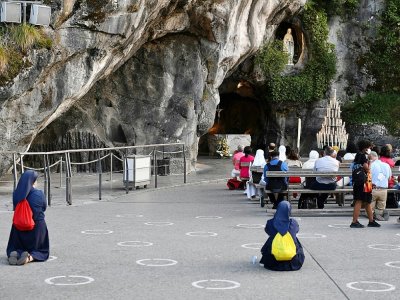 Des pélerins prient devant la Grotte du sanctuaire de Lourdes, le 14 août 2020  dans les Hautes-Pyrénées - GEORGES GOBET [AFP]