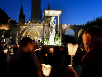 Des pèlerins, masqués, assistent à une procession aux flambeaux à Lourdes, le 14 août 2020 - GEORGES GOBET [AFP]