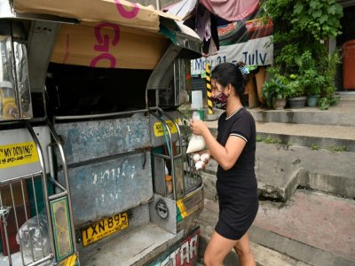 La femme de Daniel Flores, chauffeur de jeepney mis au chômage par le confinement, apporte des oeufs et du riz pour le déjeuner de la famille, le 12 août 2020 à Manille, aux Philippines - Ted ALJIBE [AFP]