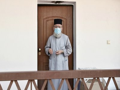 Un prêtre portant un masque se tient à la porte d'une maison de retraite à Thessalonique, le 10 août 2020 où une douzaine de résidents ont été diagnostiqués positifs au Covid-19 - Sakis MITROLIDIS [AFP]
