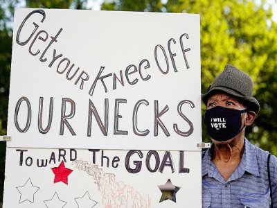 Walter Carter, 74 ans, venu de Gainesville, en Foride, porte une affiche "Enlevez votre genou de nos cous" pour une grande marche antiraciste à Washington le 28 août 2020 - Jacquelyn Martin [POOL/AFP]