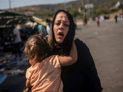 Une femme et sa fillette se sauvent après des heurts entre migrants et policiers dans le camp de réfugiés près de Mitylène sur l'île de Lesbos, le 12 septembre 2020 - ANGELOS TZORTZINIS [AFP]
