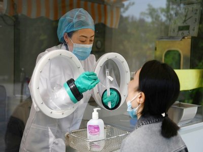Une technicienne (g) prélève un échantillon sur une employée de la société de biotechnologie chinoise Coyote qui fabrique le Flash 20, une machine de dépistage rapide du coronavirus - GREG BAKER [AFP]