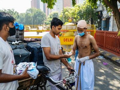 Des bénévoles, dont un habillé comme le héros de l'indépendance indienne, le Mahatma Gandhi, dont c'est l'anniversaire, distribuent des masques aux conducteurs de vélos-taxis, à New Delhi le 2 octobre 2020 - Jewel SAMAD [AFP]