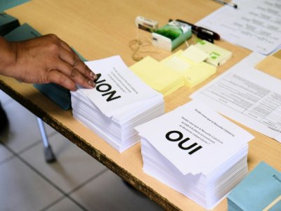 Une personne prend les bulletins avant de voter au référendum sur l'indépendance de la Nouvelle-Calédonie, le 4 octobre 2020 dans un bureau à Nouméa - Theo Rouby [AFP]