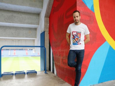Seb Toussaint a peint plus de 365 m2 de fresques au sein de la tribune Borelli du Stade d'Ornano à Caen. Le T-shirt qu'il porte est aussi le fruit d'une de ses créations.