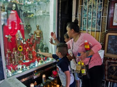 Une femme et ses enfants touchent une vitre devant une représentation de la "Santa Muerte" dans une rue du quartier de Tepito, le 1er octobre 2020 à Mexico - CLAUDIO CRUZ [AFP]