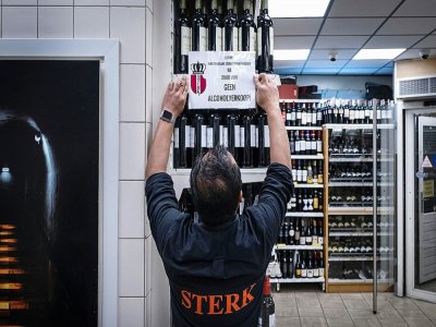 Un gérant de magasin colle une affiche indiquant que la vente d'alccol est interdite après 20h, le 14 octobre 2020 à Amsterdam, aux Pays-Bas - Ramon van Flymen [ANP/AFP]