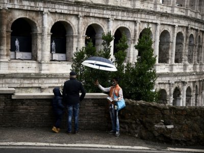 Un vendeur de rue et des passants devant le Colisée à Rome le 16 octobre 2020 - Filippo MONTEFORTE [AFP]