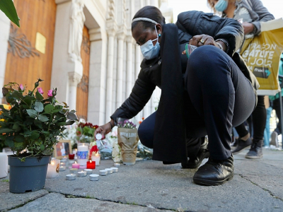 Une femme allume une bougie devant la basilique Notre-Dame à Nice lors d'un hommage aux victimes de l'attentat, le 30 octobre 2020 - Valery HACHE [AFP]